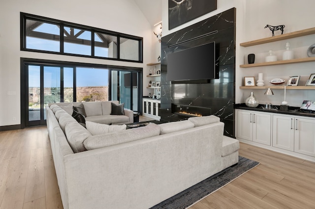 living room featuring light wood-type flooring, a towering ceiling, and a high end fireplace