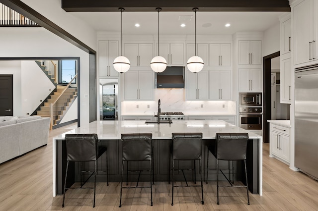 kitchen with built in appliances, white cabinetry, pendant lighting, a breakfast bar, and a large island with sink