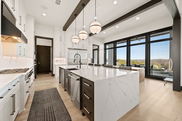 kitchen featuring decorative light fixtures, white cabinetry, a center island with sink, beamed ceiling, and stainless steel appliances