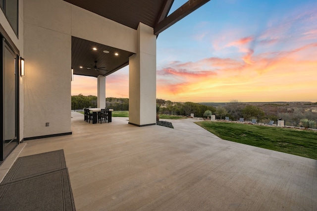 patio terrace at dusk featuring ceiling fan and a lawn