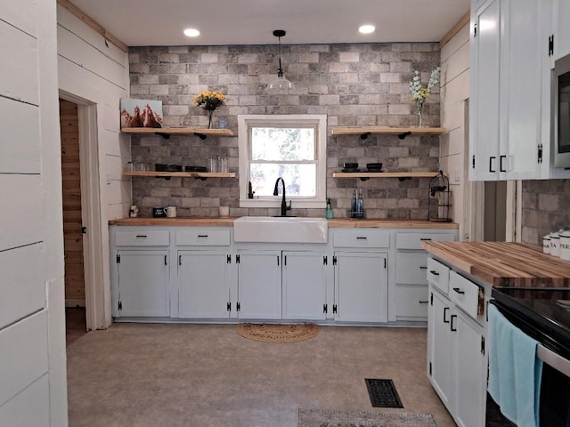 kitchen with butcher block countertops, sink, white cabinetry, and pendant lighting