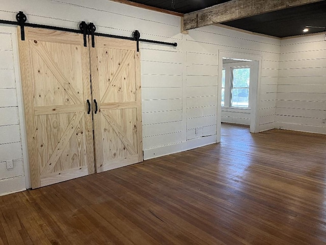 interior space featuring beam ceiling, a barn door, and dark wood-type flooring