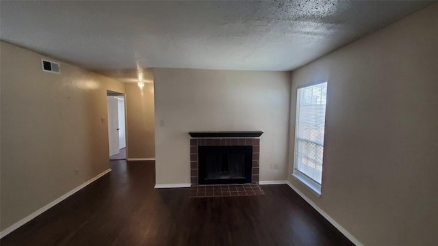 unfurnished living room featuring dark wood-type flooring, a textured ceiling, and a tiled fireplace