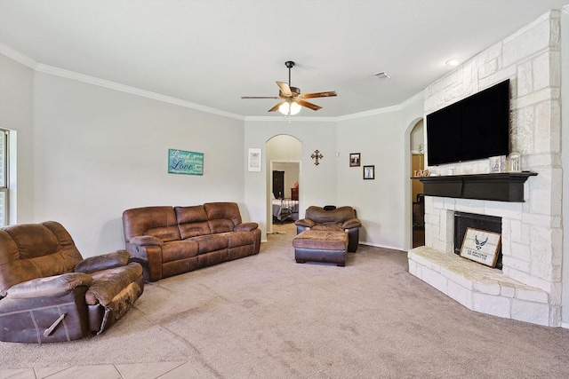 living room featuring ceiling fan, a stone fireplace, carpet floors, and crown molding