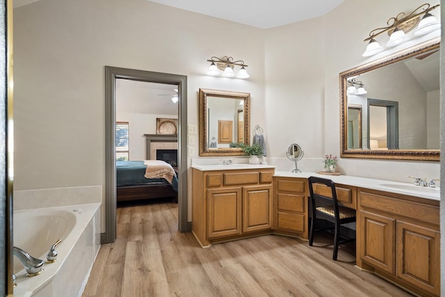 bathroom featuring a tiled fireplace, hardwood / wood-style flooring, a tub to relax in, and vanity