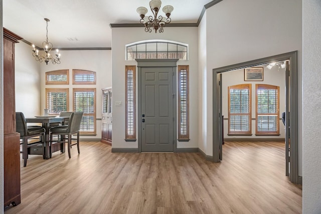 foyer entrance featuring crown molding, an inviting chandelier, a towering ceiling, and light hardwood / wood-style floors