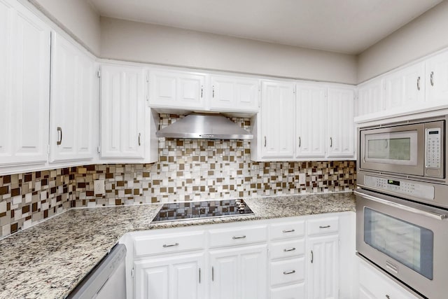 kitchen with wall chimney exhaust hood, white cabinets, appliances with stainless steel finishes, and decorative backsplash