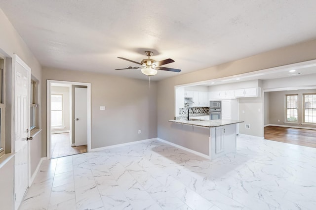 kitchen featuring white cabinetry, sink, backsplash, kitchen peninsula, and stainless steel microwave