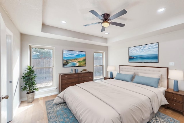 bedroom featuring light wood-type flooring, multiple windows, ceiling fan, and a raised ceiling