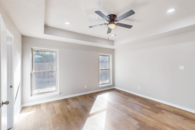 spare room featuring wood-type flooring, ceiling fan, and a raised ceiling