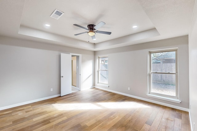 empty room featuring light wood-type flooring, ceiling fan, and a raised ceiling