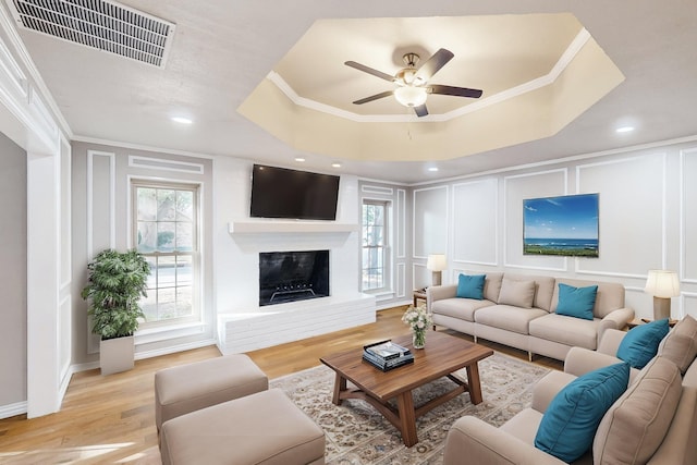 living room with light wood-type flooring, a tray ceiling, and ornamental molding