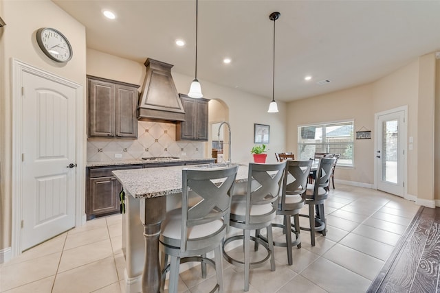 kitchen with pendant lighting, a breakfast bar, an island with sink, and custom exhaust hood