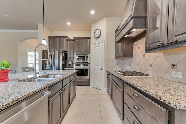 kitchen with sink, appliances with stainless steel finishes, premium range hood, dark brown cabinets, and ornamental molding