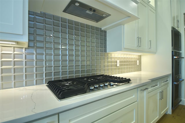 kitchen with tasteful backsplash, black gas stovetop, exhaust hood, white cabinets, and light stone counters