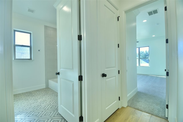 corridor with light wood-type flooring and crown molding