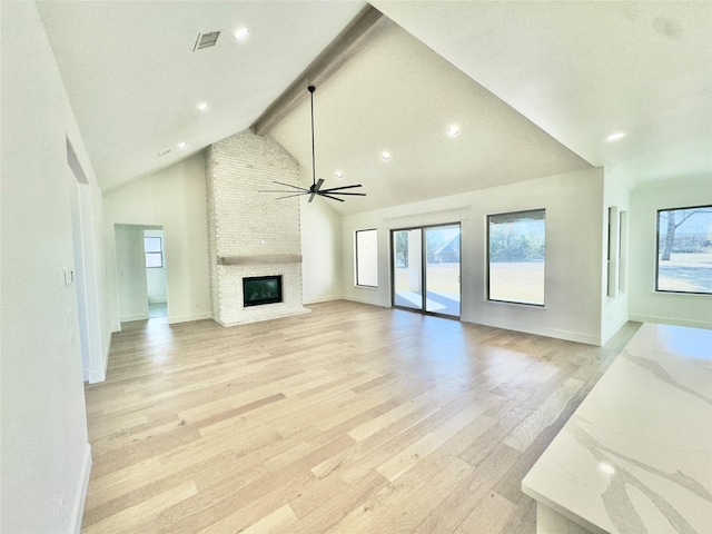 unfurnished living room with ceiling fan, lofted ceiling with beams, a fireplace, and light hardwood / wood-style floors