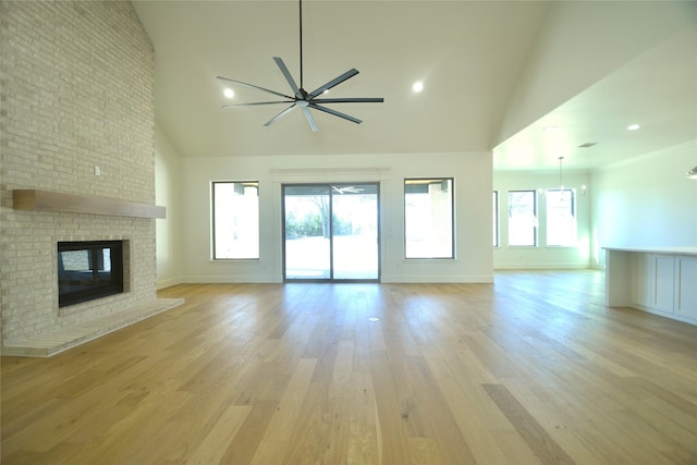 unfurnished living room with light hardwood / wood-style floors, a towering ceiling, ceiling fan, and a fireplace