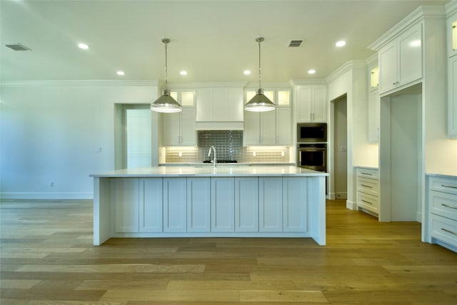 kitchen with white cabinets, hanging light fixtures, appliances with stainless steel finishes, and an island with sink