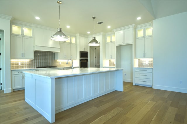 kitchen with white cabinetry, black appliances, pendant lighting, and a kitchen island with sink