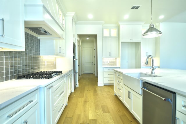 kitchen with pendant lighting, sink, white cabinetry, stainless steel appliances, and custom range hood