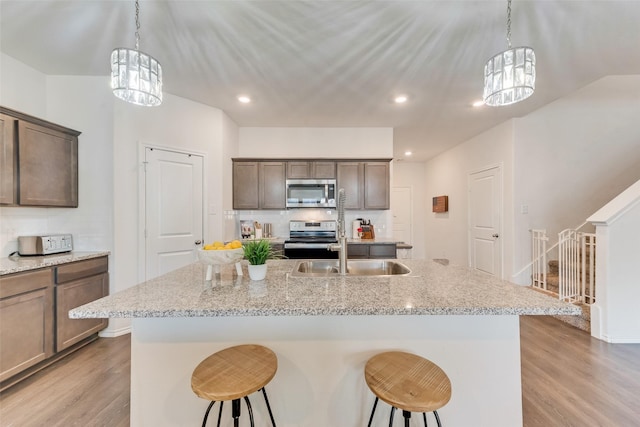 kitchen with light hardwood / wood-style floors, stainless steel appliances, an island with sink, and light stone counters