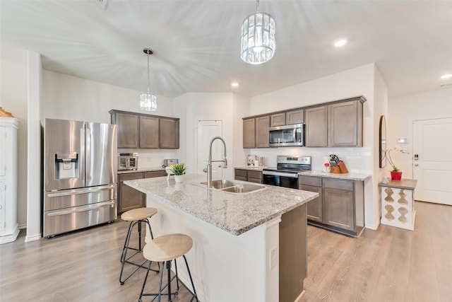 kitchen featuring a center island with sink, hanging light fixtures, stainless steel appliances, light stone countertops, and sink