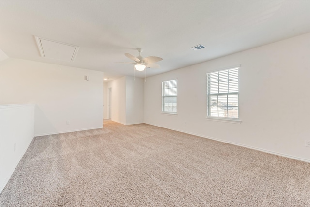 spare room with visible vents, a ceiling fan, baseboards, light colored carpet, and attic access