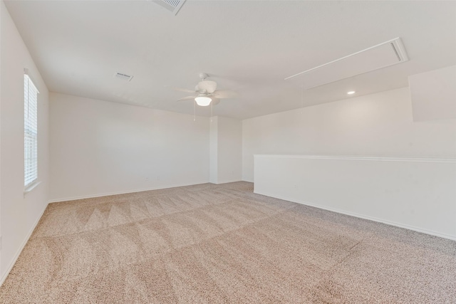 carpeted empty room with visible vents, baseboards, attic access, and ceiling fan