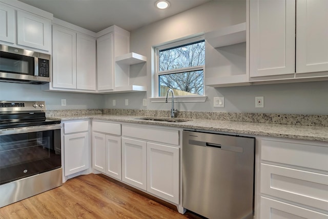 kitchen featuring white cabinetry, stainless steel appliances, light hardwood / wood-style flooring, light stone counters, and sink