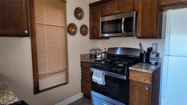 kitchen with white fridge, decorative backsplash, light stone countertops, and range with gas cooktop