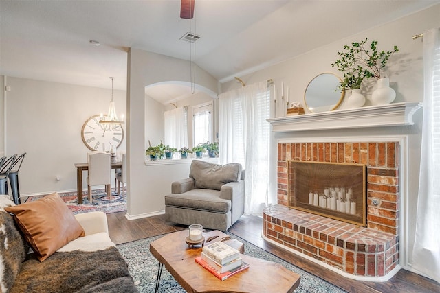 living room with a brick fireplace, dark hardwood / wood-style flooring, lofted ceiling, and an inviting chandelier