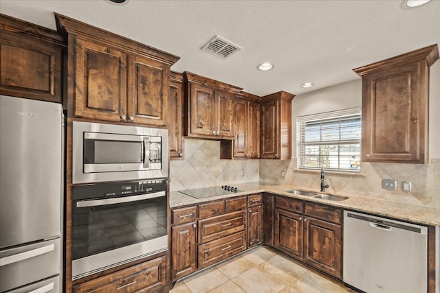 kitchen featuring appliances with stainless steel finishes, tasteful backsplash, light tile patterned flooring, light stone countertops, and sink