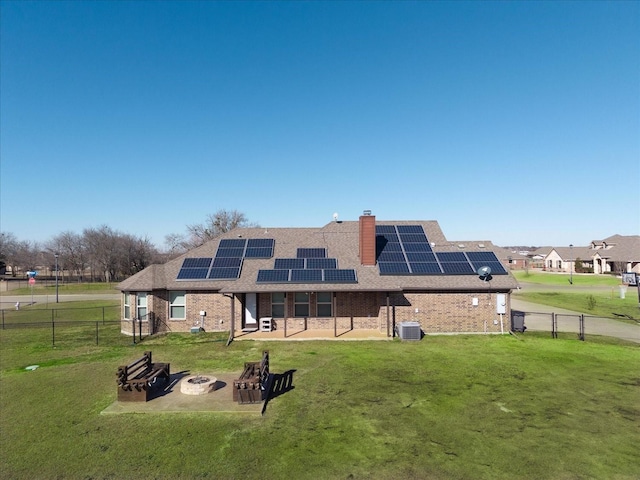 rear view of property featuring a lawn, an outdoor fire pit, central AC unit, and solar panels