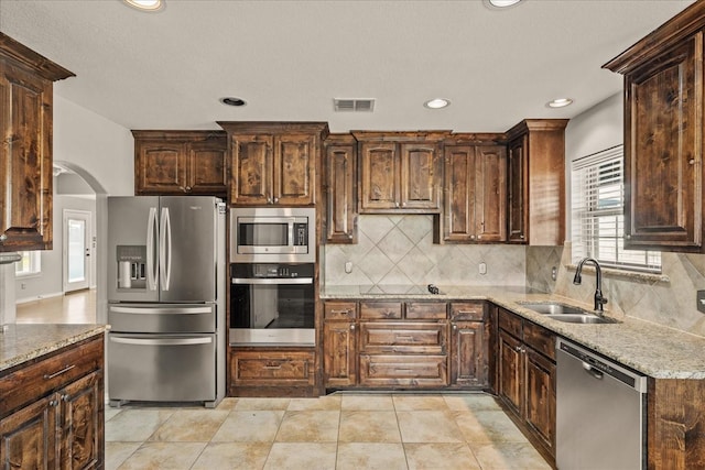 kitchen with decorative backsplash, sink, appliances with stainless steel finishes, dark brown cabinets, and light stone counters