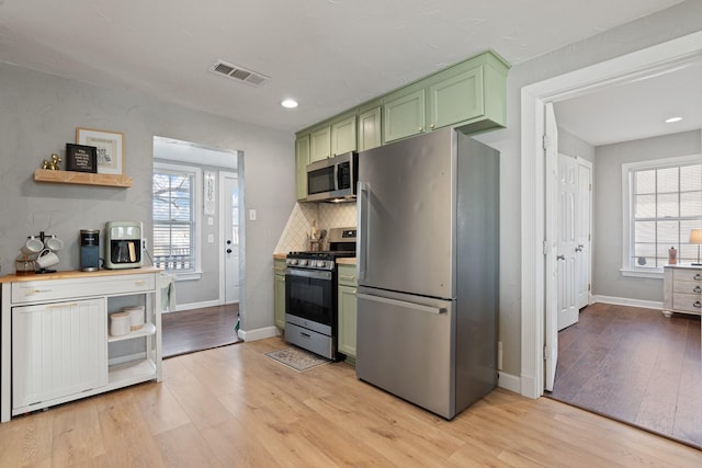 kitchen featuring green cabinetry, light wood-type flooring, a wealth of natural light, and stainless steel appliances