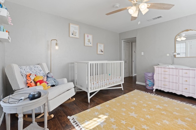 bedroom featuring ceiling fan, dark wood-type flooring, and a nursery area