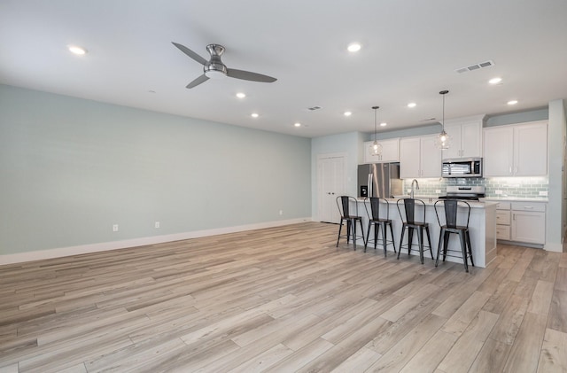 kitchen featuring pendant lighting, white cabinets, appliances with stainless steel finishes, a kitchen bar, and an island with sink