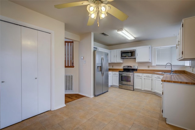 kitchen featuring white cabinets, wooden counters, stainless steel appliances, sink, and ceiling fan