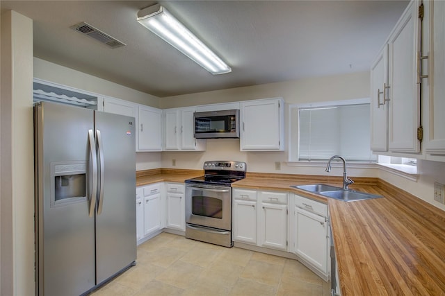 kitchen featuring appliances with stainless steel finishes, white cabinetry, wooden counters, and sink