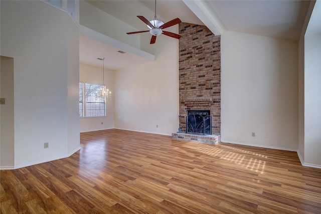 unfurnished living room with ceiling fan with notable chandelier, beamed ceiling, high vaulted ceiling, a brick fireplace, and light hardwood / wood-style flooring