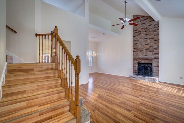 unfurnished living room featuring a fireplace, beamed ceiling, light wood-type flooring, high vaulted ceiling, and ceiling fan with notable chandelier