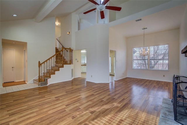 unfurnished living room featuring hardwood / wood-style flooring, a high ceiling, beamed ceiling, and ceiling fan with notable chandelier