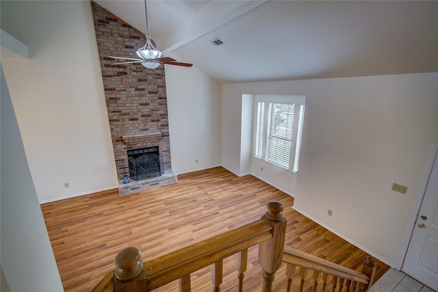 living room with a fireplace, light hardwood / wood-style flooring, ceiling fan, and vaulted ceiling with beams