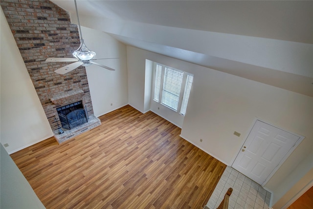 unfurnished living room with light wood-type flooring, vaulted ceiling, a fireplace, and ceiling fan