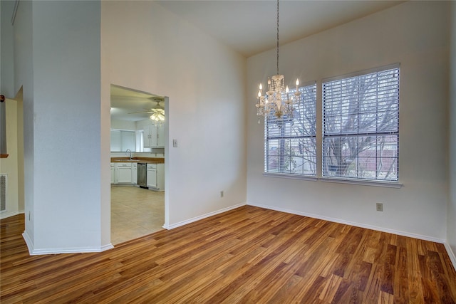 unfurnished dining area featuring ceiling fan with notable chandelier, sink, a wealth of natural light, and light hardwood / wood-style flooring