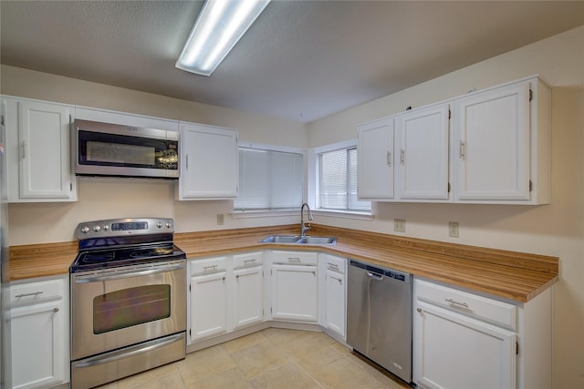 kitchen with sink, white cabinetry, light tile patterned floors, and stainless steel appliances