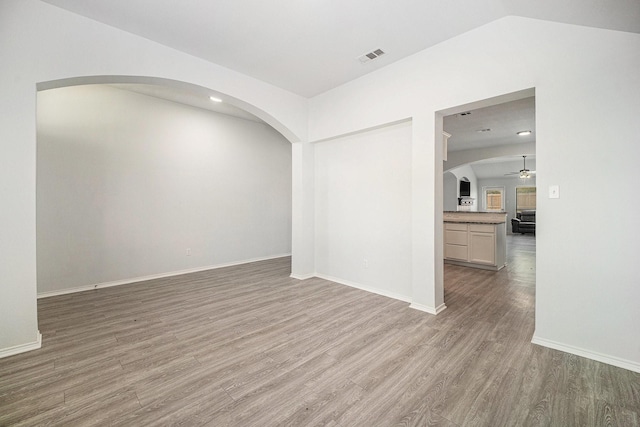 empty room with arched walkways, a ceiling fan, visible vents, wood finished floors, and lofted ceiling