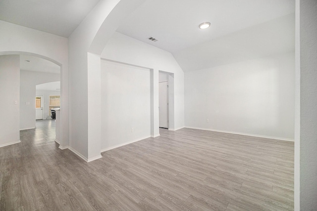 spare room featuring arched walkways, wood finished floors, baseboards, and vaulted ceiling