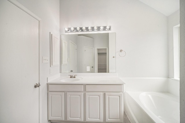 bathroom with a closet, a bath, and vanity